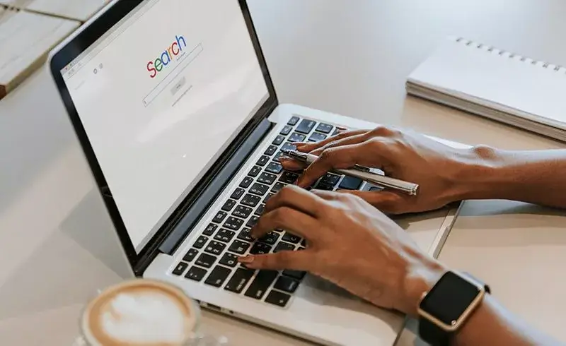 Person with iwatch typing on computer next to coffee