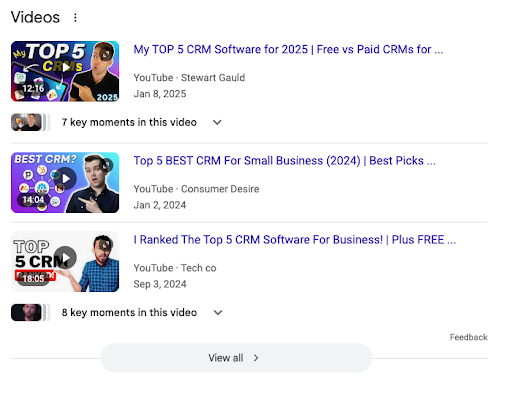 Screenshot of three YouTube video search results about top CRM software, featuring presenters, titles, channels, views, and publish dates—highlighting options ideal for social media marketing for business. A "View all" button appears at the bottom.
