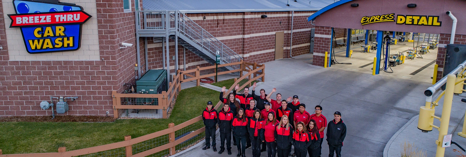 A group of employees in red and black uniforms standing in front of a car wash facility with signs reading "breeze thru car wash" and "express detail.