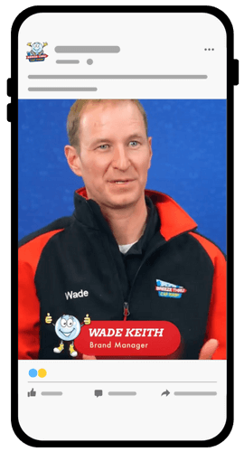 A man wearing a black and red jacket with the name "Wade" is shown on a phone screen. The caption reads "WADE KEITH, Brand Manager" with a cartoon mascot beside the text.