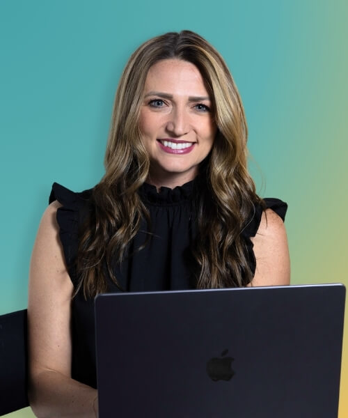 A woman with long brown hair and a black top smiles while sitting behind an open laptop against a blue-green gradient background.